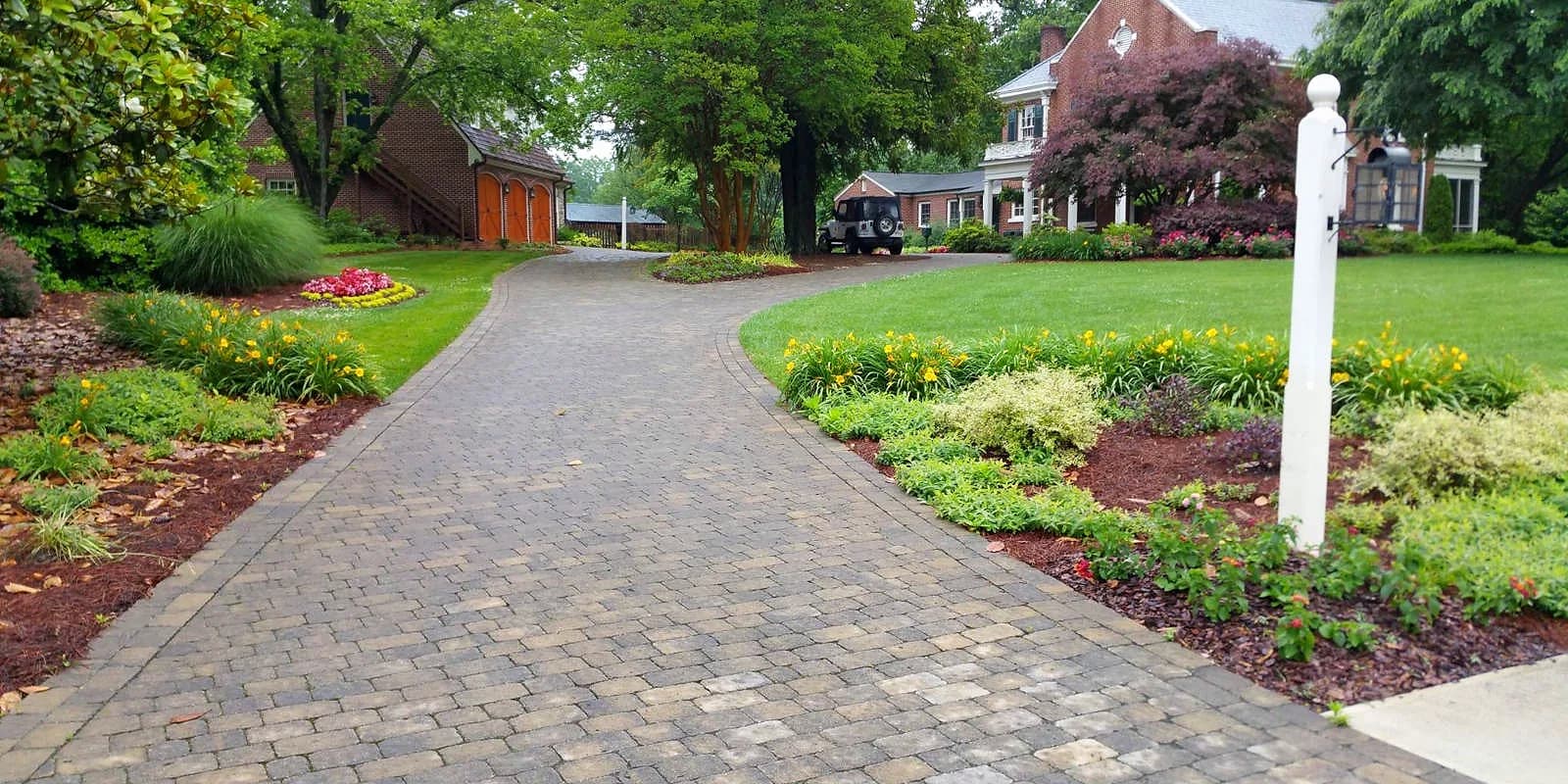 Long paver driveway between flower beds and a lamppost