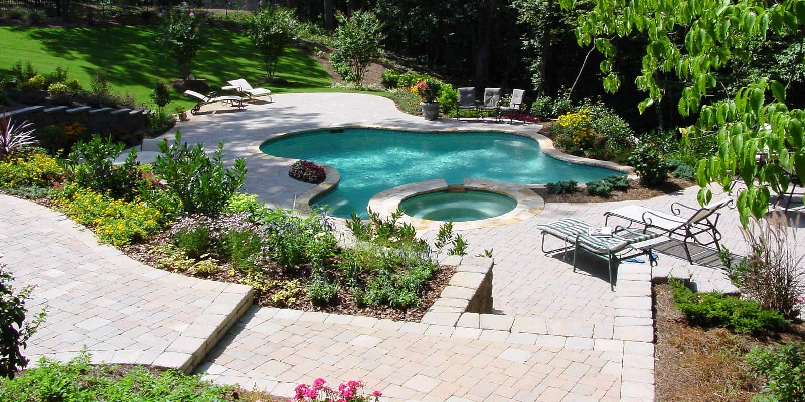 Curved pool and spa surrounded by paver deck and plantings