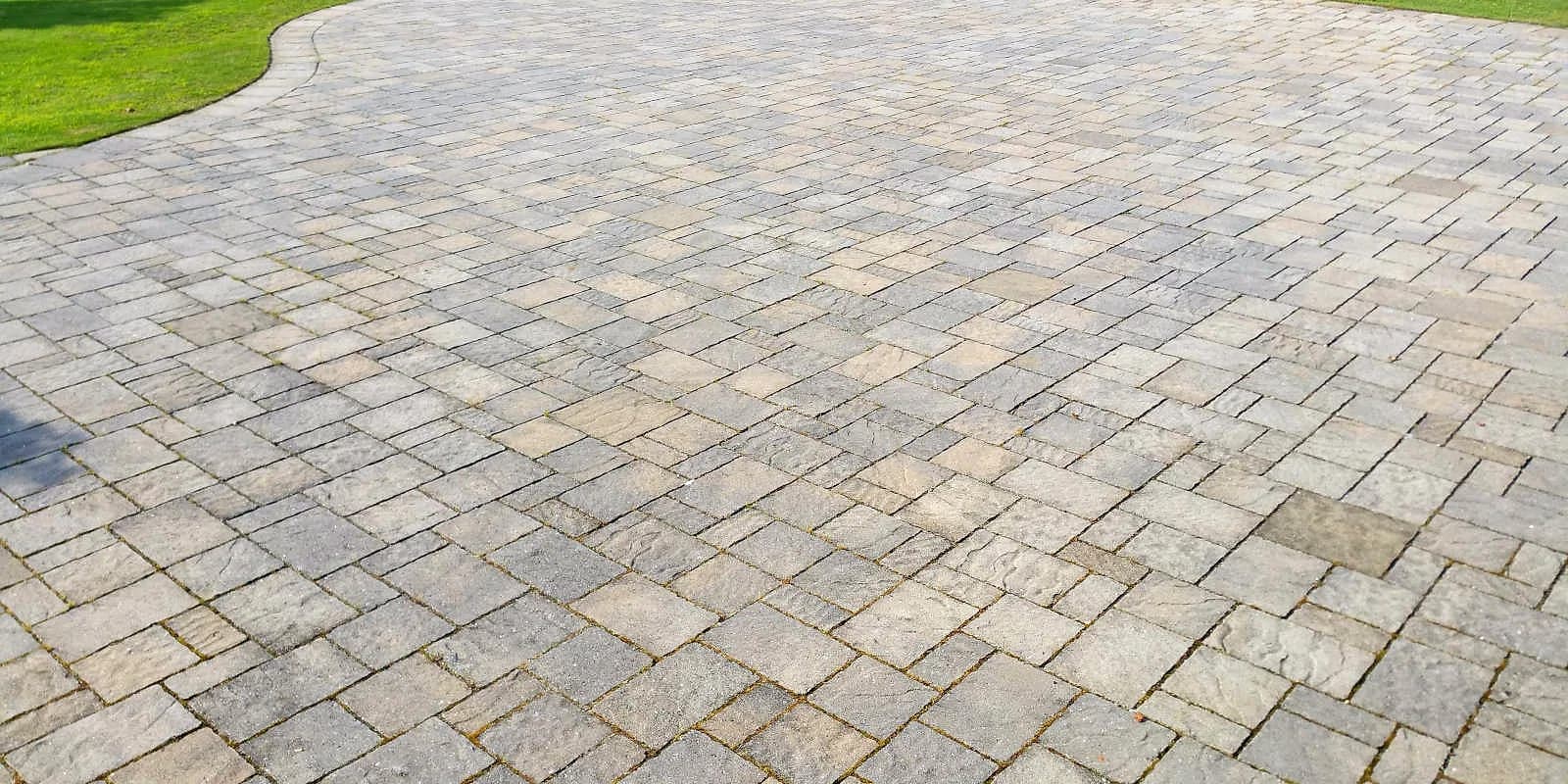 Close view of a gray paver surface curving along a lawn