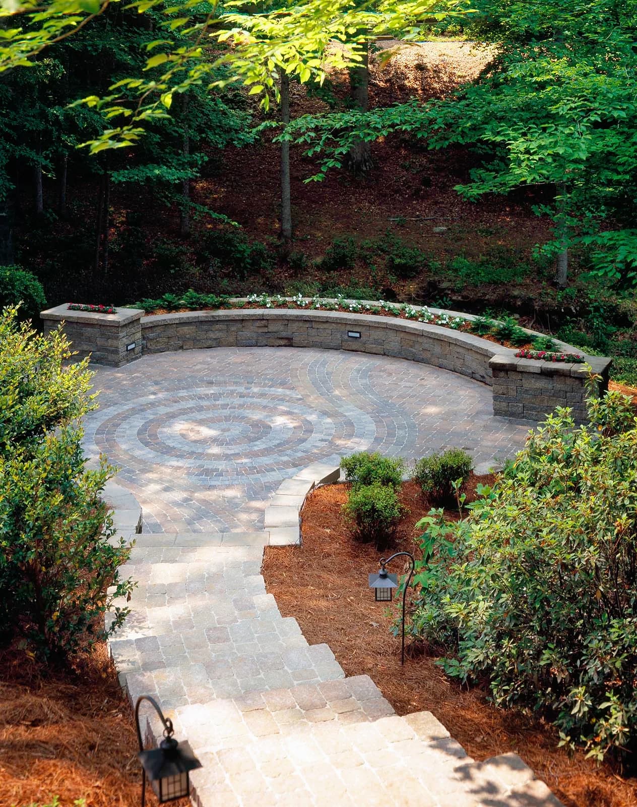 Round paver patio with a curved seat wall at the end of a paver path
