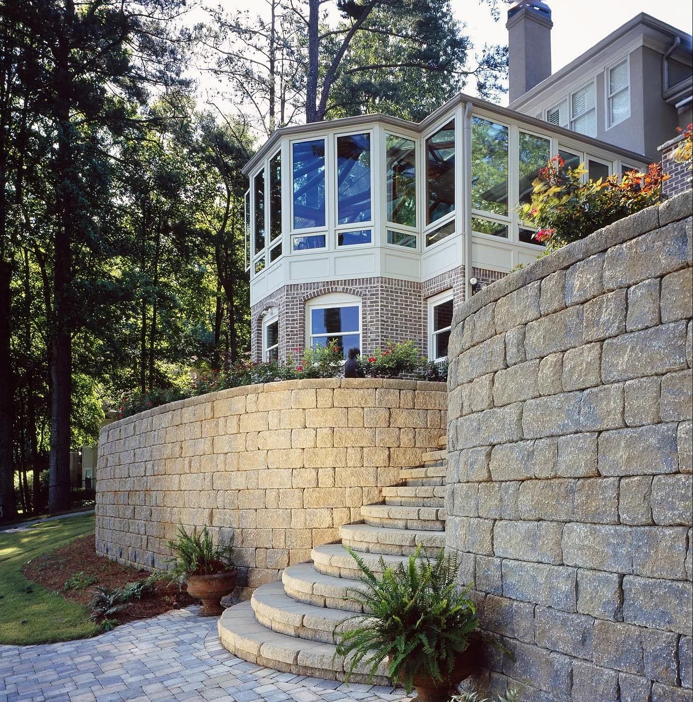 Tall block retaining wall with curved stone steps below a house