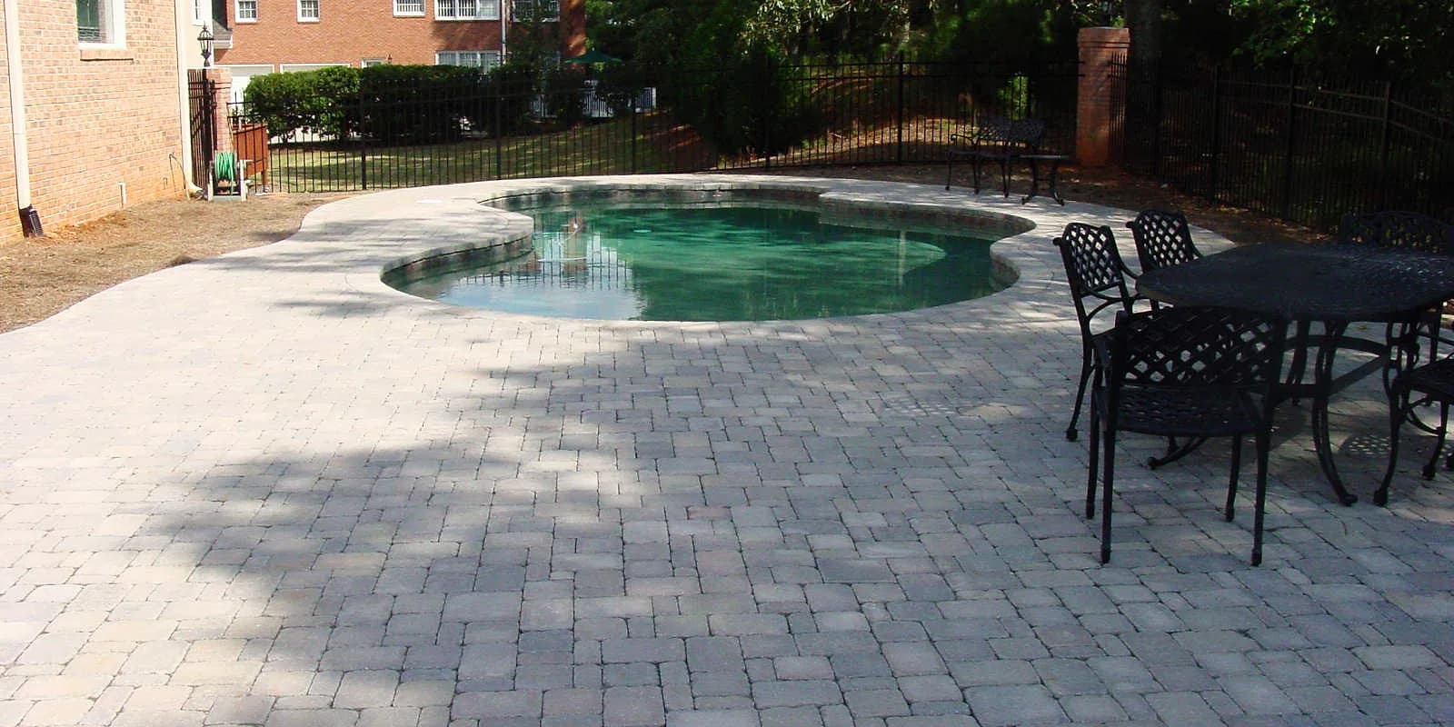 Paver pool deck with a dining table beside a small pool