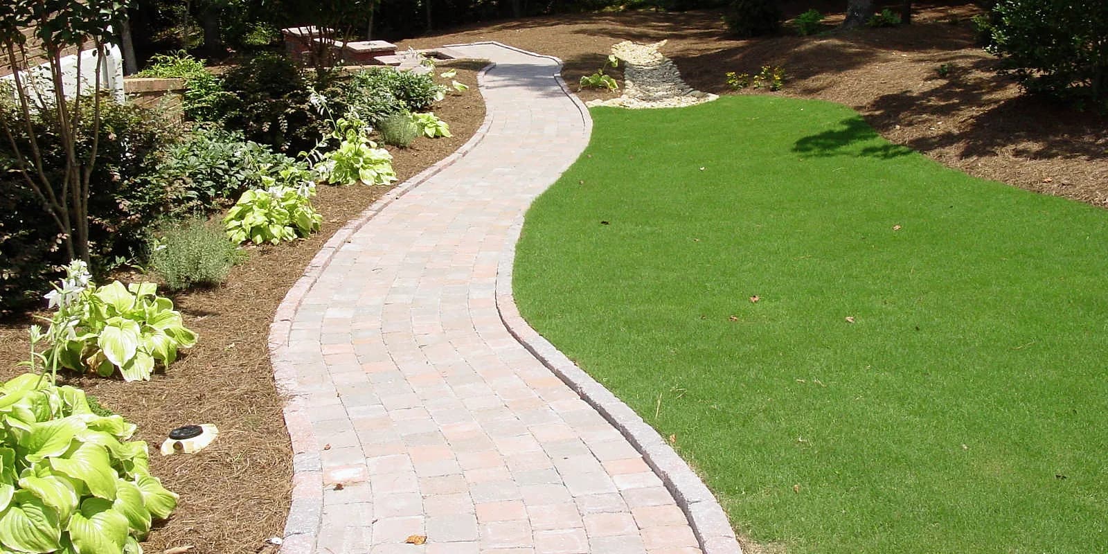 Narrow paver walkway curving between lawn and shade plantings