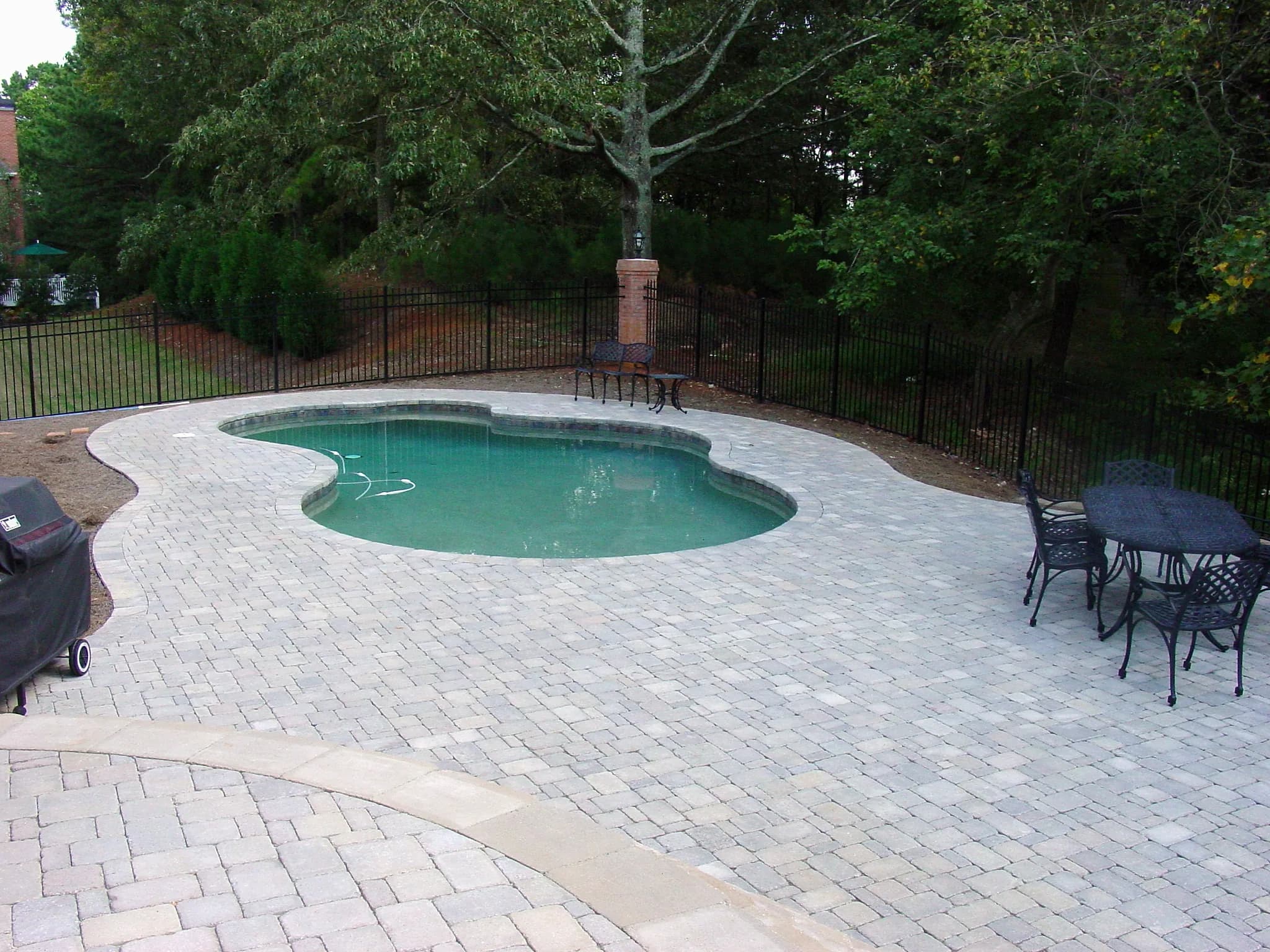 Light paver pool deck around a freeform pool with a fence behind